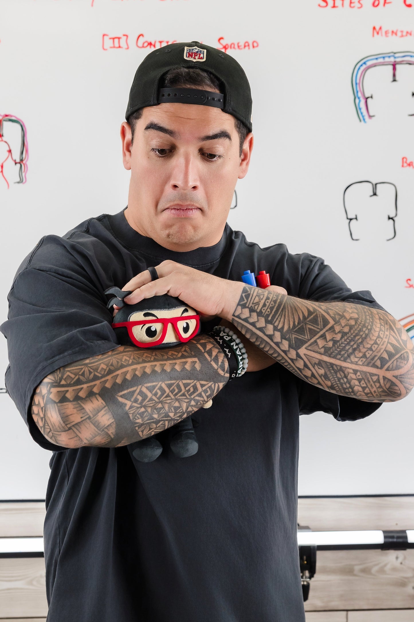 Person with tattoos holding a small ninja plush toy in front of medical educational diagrams on a whiteboard.